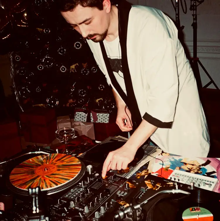 A man DJ'ing and leaning over his setup